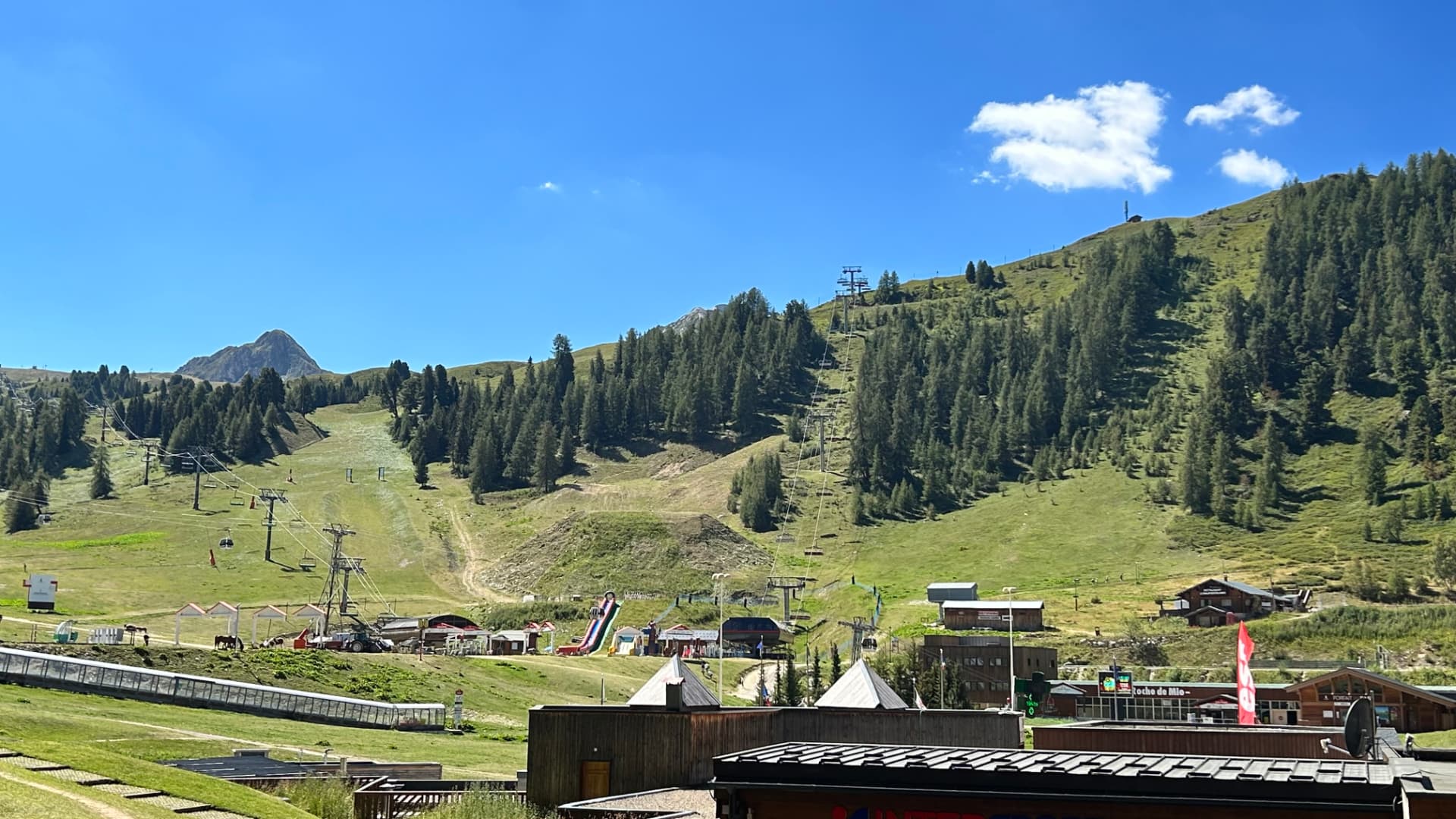 Vue depuis le balcon en été : alpages verdoyants, mélèzes et remontées mécaniques