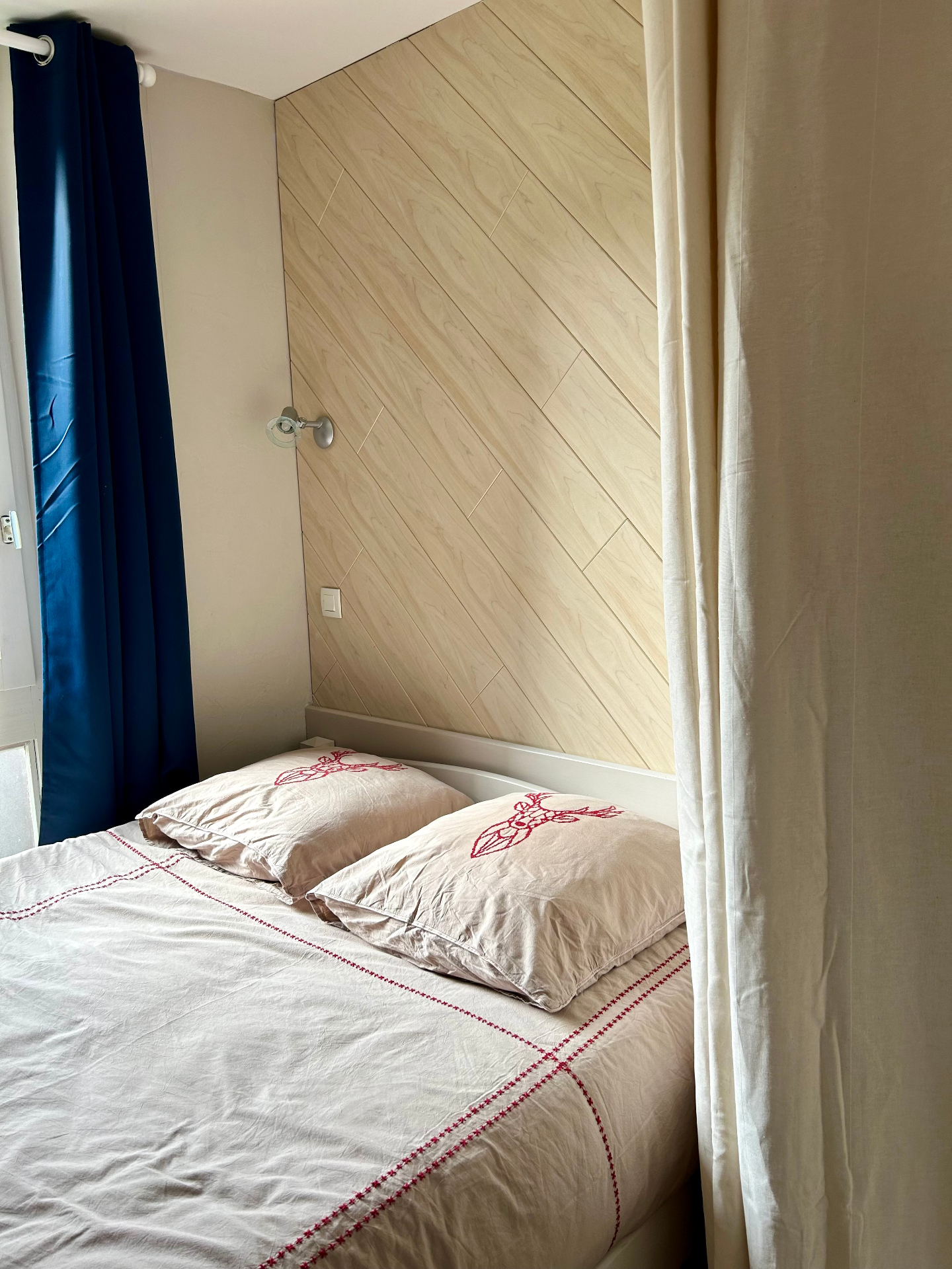 Lit double avec tête de lit en bois clair et couette brodée de motifs rouges