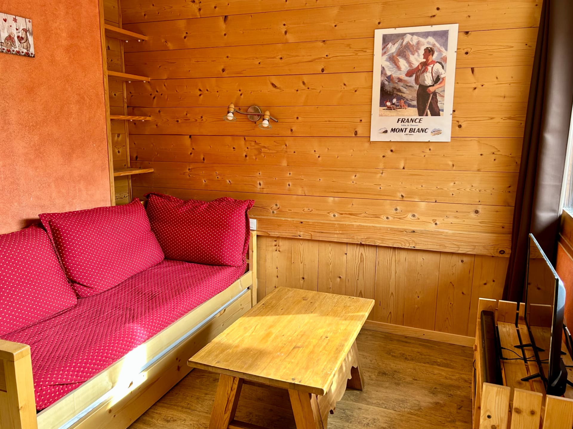 Salon en lambris avec banquette rouge à pois, table basse en bois et affiche Mont-Blanc