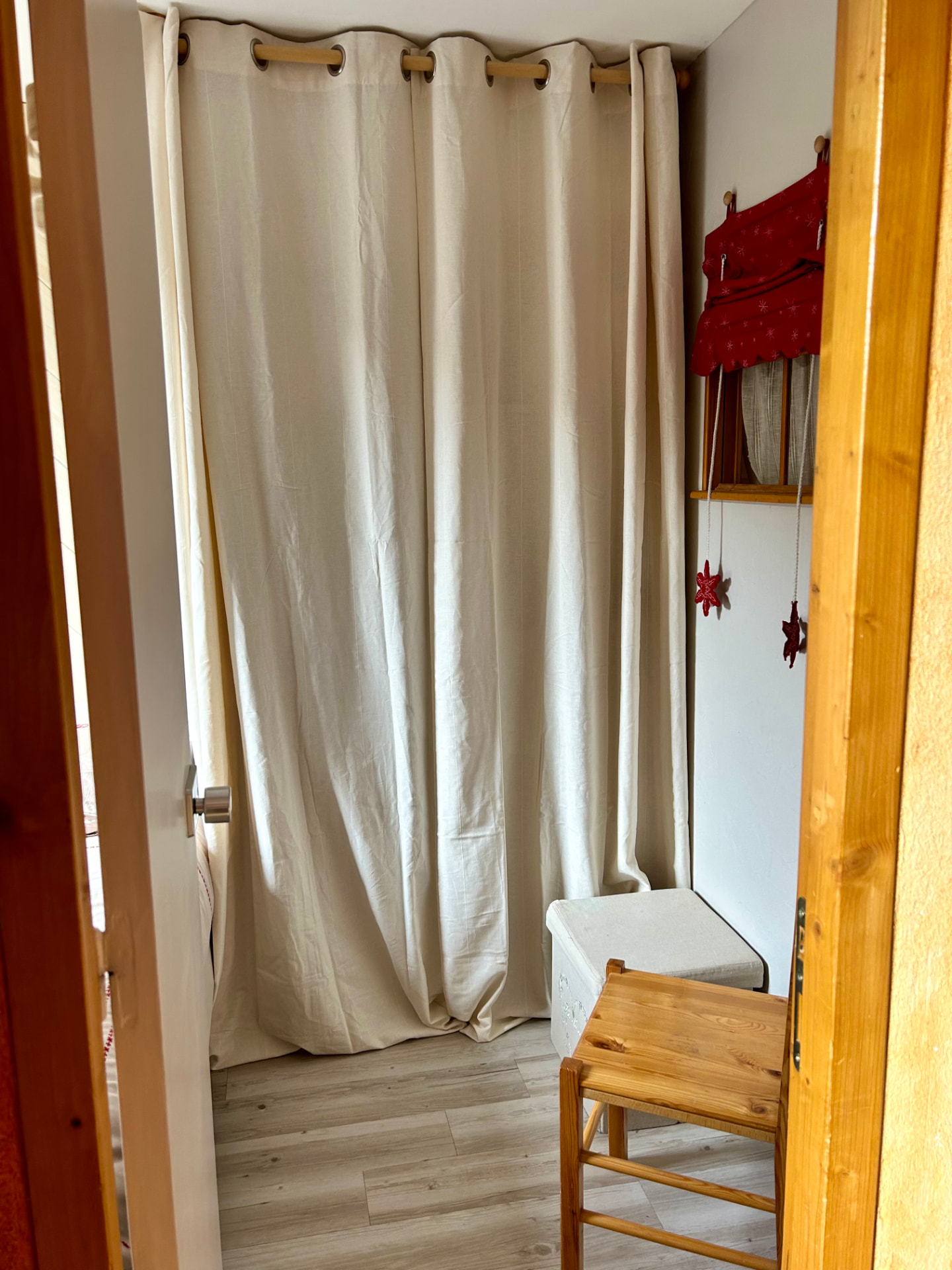 Coin nuit de la chambre avec rideaux en lin, tabouret en bois et décoration montagnarde rouge