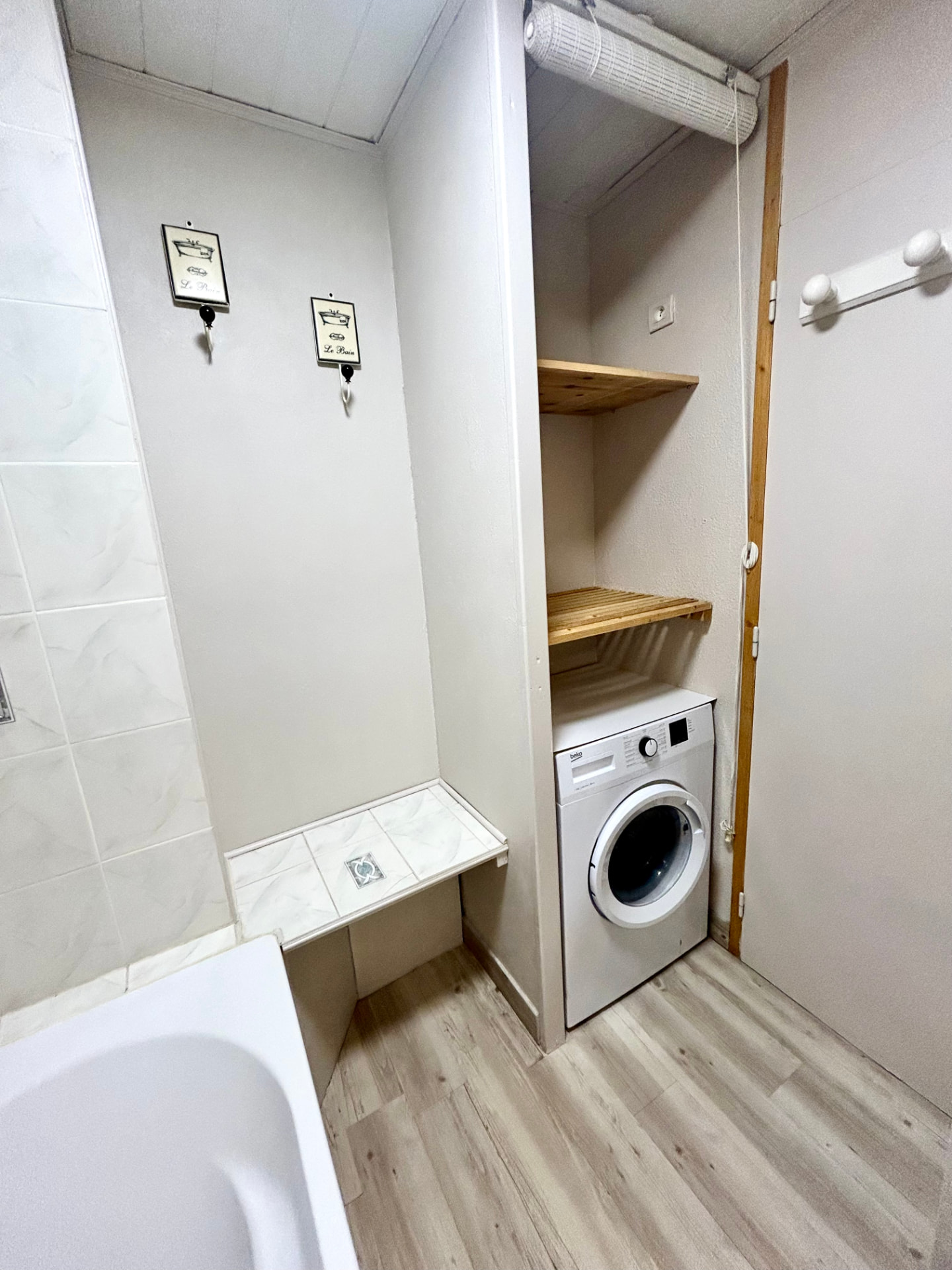Salle de bain avec baignoire, lave-linge et étagères en bois
